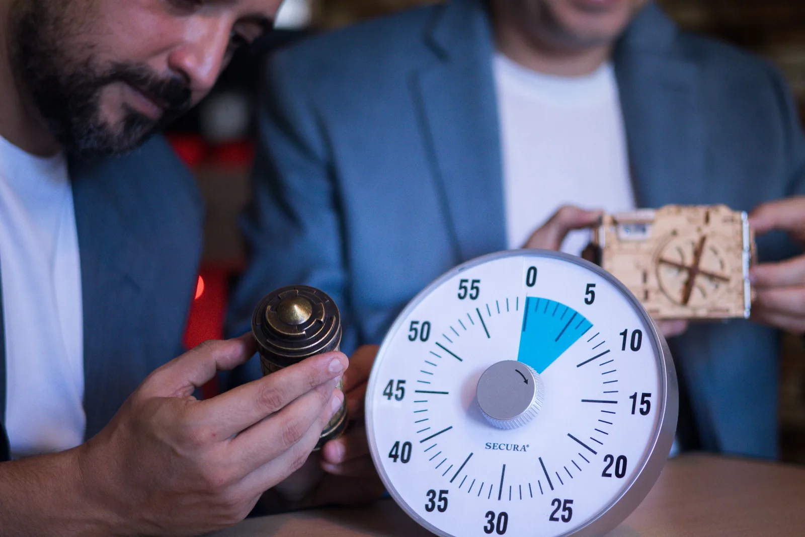 Two men solve puzzles collaboratively, timed by a Secura timer. Focused teamwork. Corporate team building escape room pricing: the line items to quote