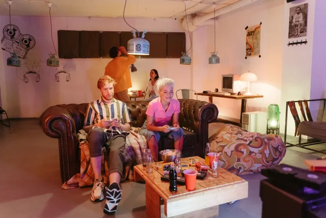 Four friends play retro video games indoors on a leather sofa, creating a cozy, nostalgic atmosphere. The escape room business plan: sections that matter