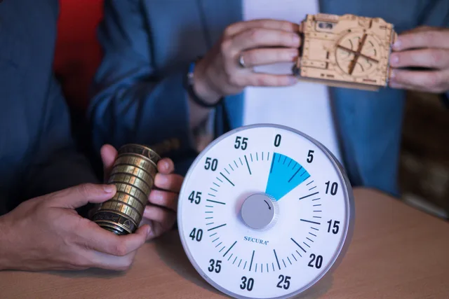 Close-up of hands holding puzzle lock and timer in escape room setting. Hiring and training escape room game masters: duties, flow and reset time