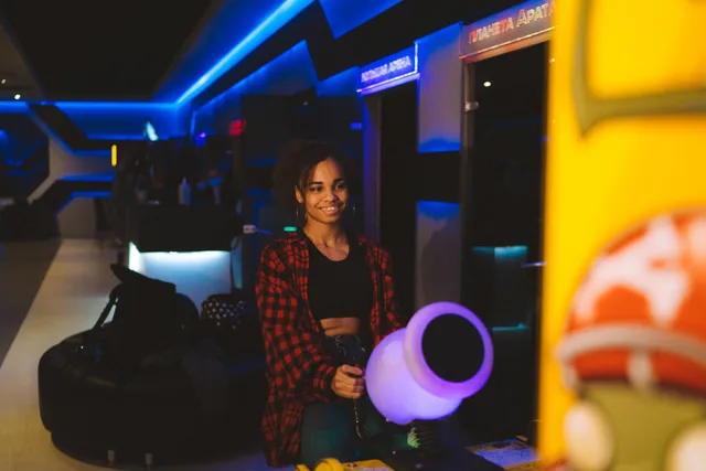 A woman enjoys playing an arcade game in a neon-lit setting, smiling at the gaming machine. How to hire reliable escape room staff without wasting a whole season